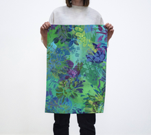 Load image into Gallery viewer, A person holding a tea towel with a vibrant multicolored floral pattern on a white background.